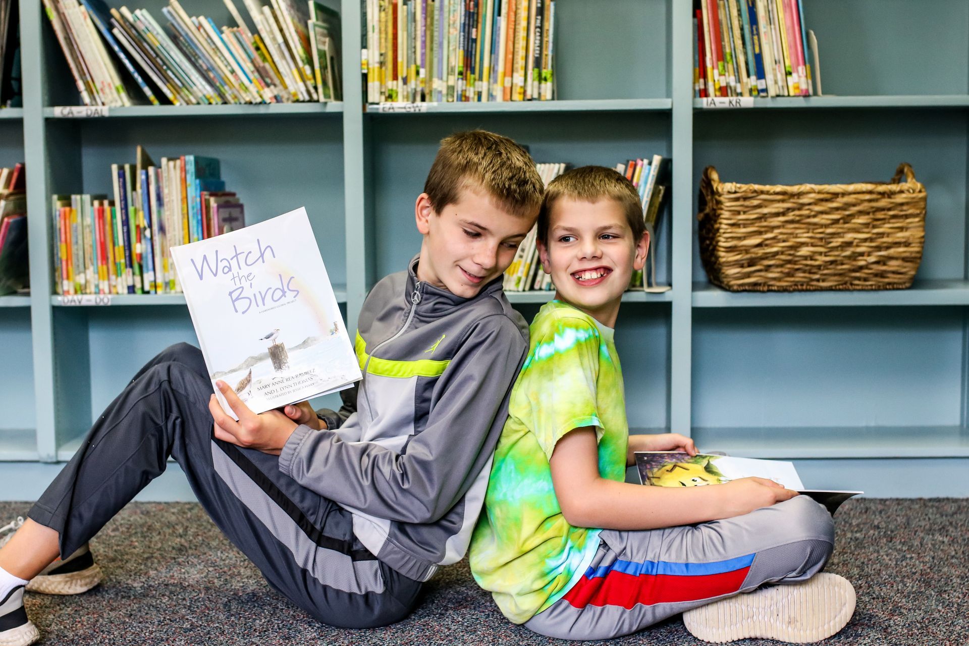 Programs for Refugees: Two young boys are sitting back to back reading a book in a library.
