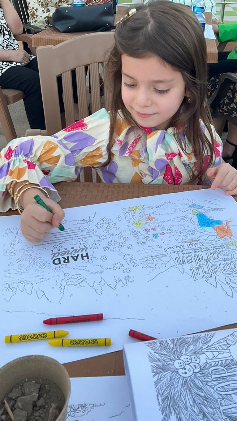 CRT: A little girl is sitting at a table drawing on a piece of paper.