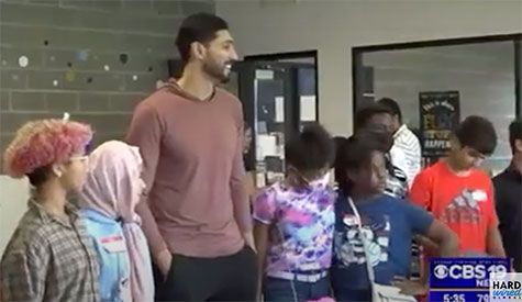 Non Profit: A man is standing next to a group of children in a room.