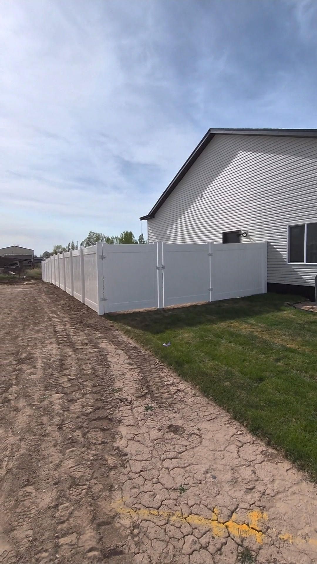 White vinyl privacy fence along a sidewalk beside a grassy verge in a residential neighborhood