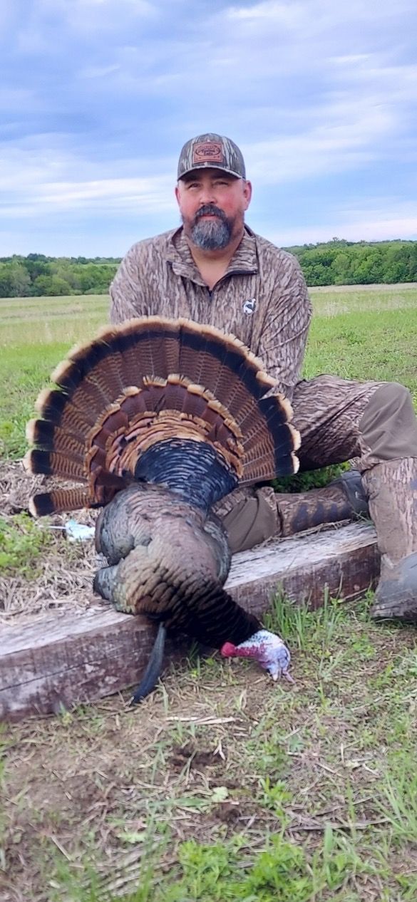 A man is holding a large Kansas turkey in a field.