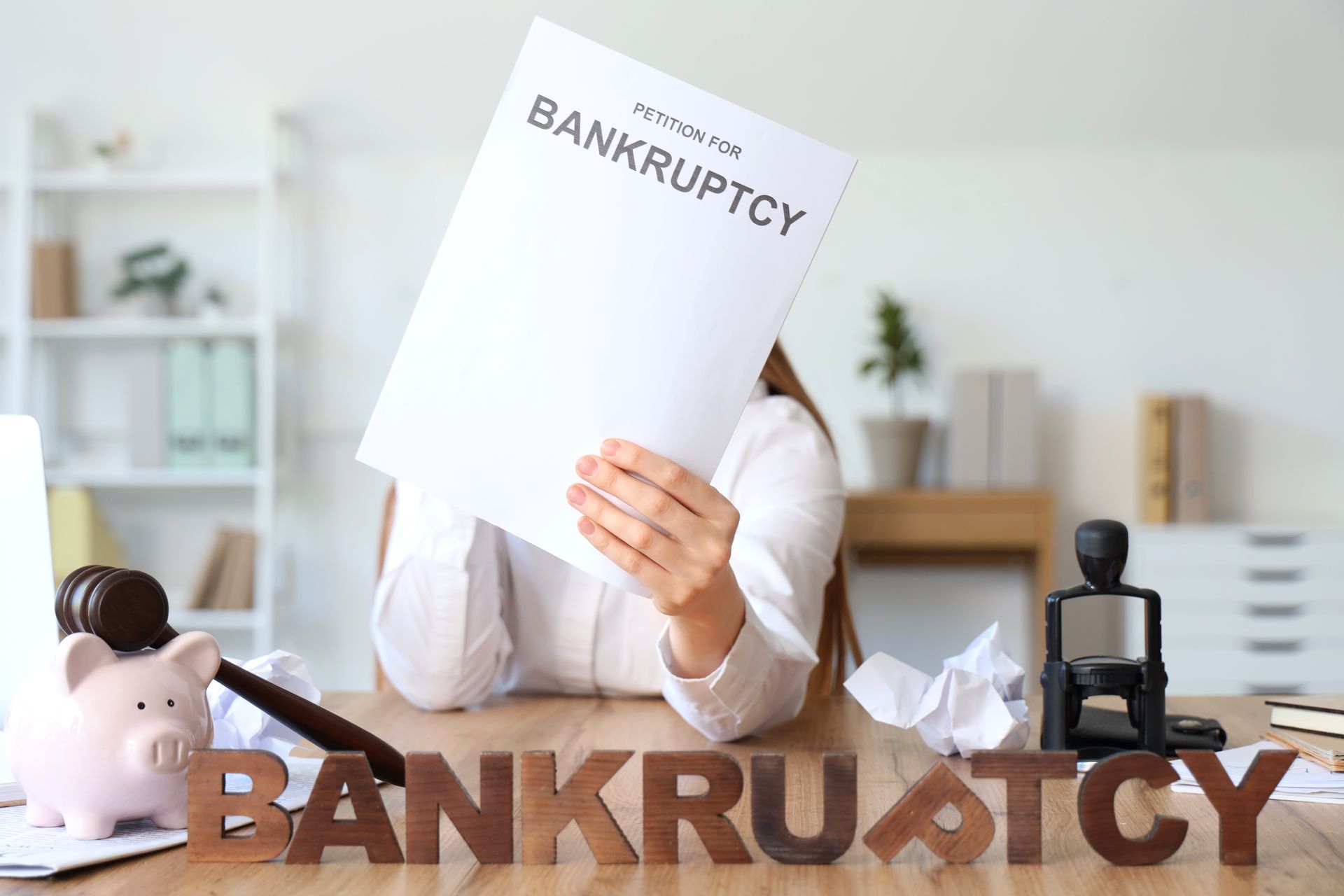 Woman holding bankruptcy document, desk with gavel, pig, and word 