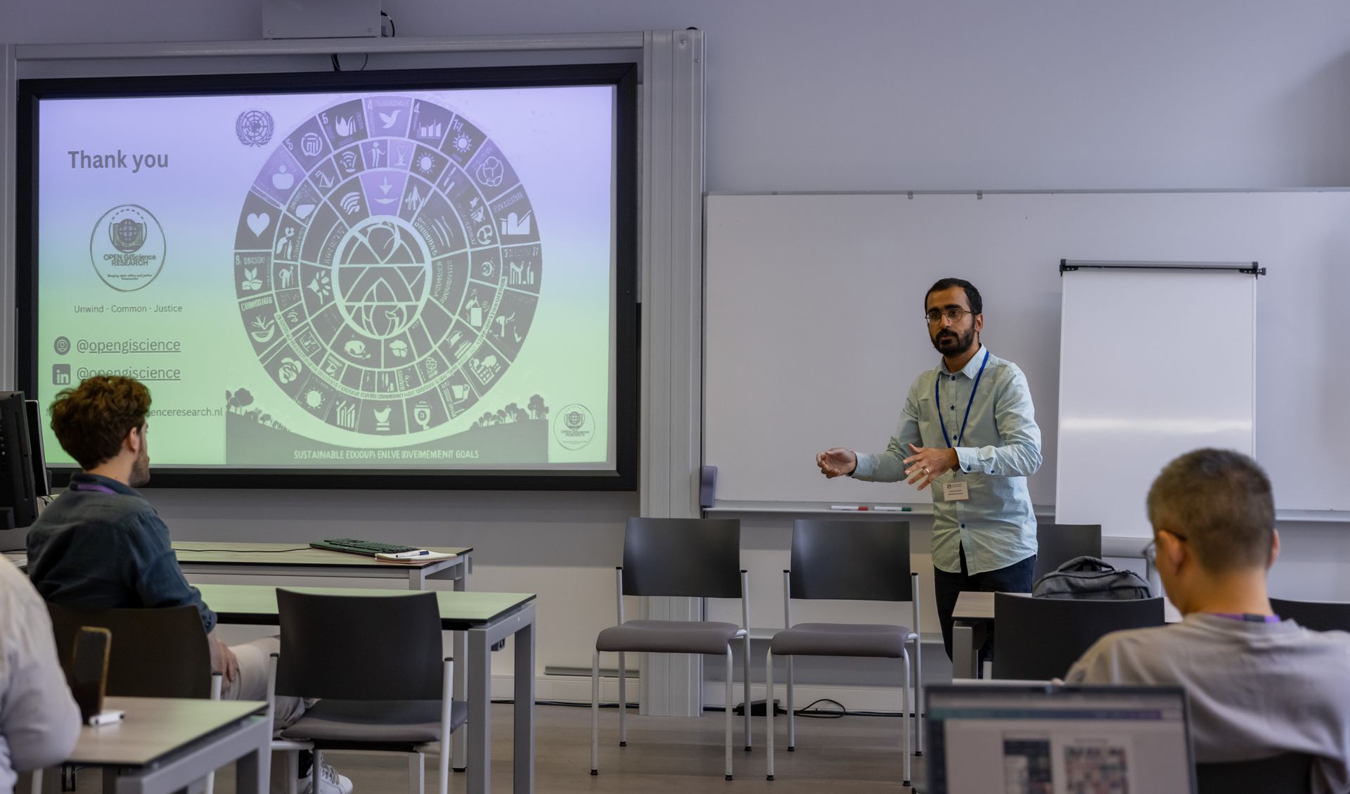 Man giving presentation with circular graphic on screen, in a classroom setting.
