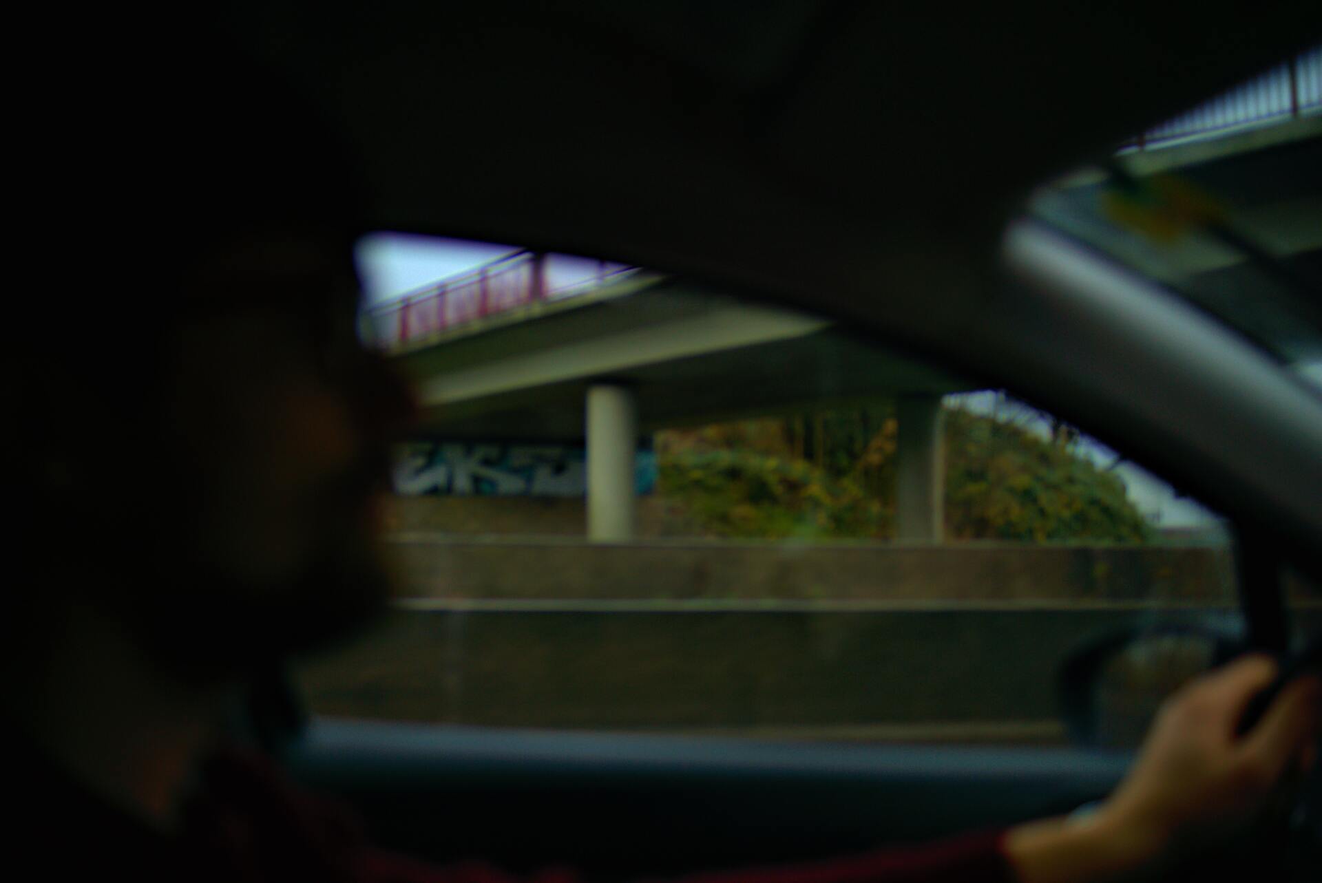 Blurred view from a car window of a person driving on a road. A bridge over the road is visible.