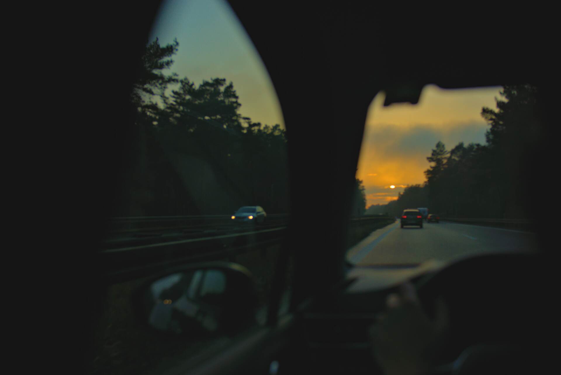 View from a car window at dusk, with headlights on the road.