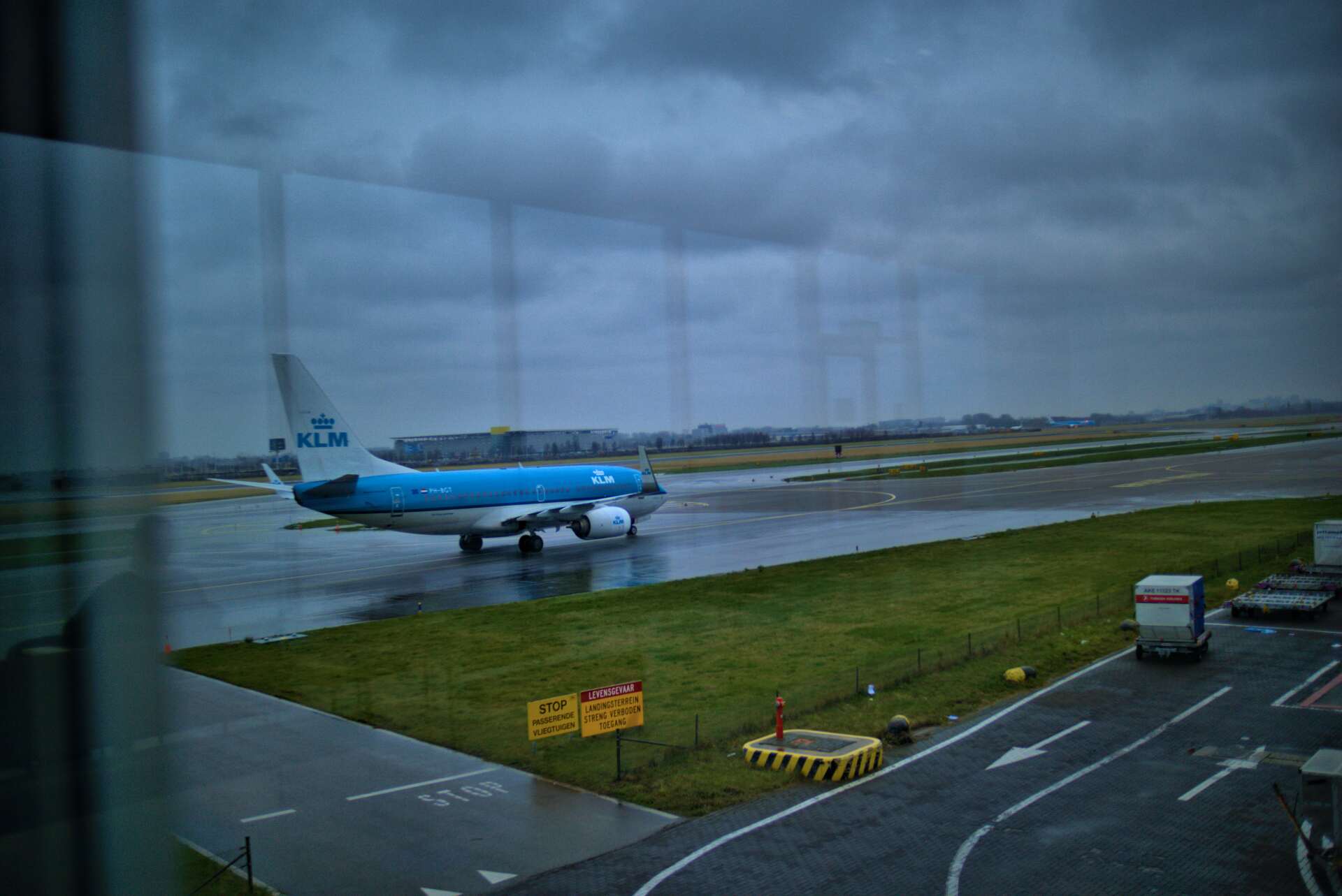 KLM airplane on wet runway at an airport, overcast sky.
