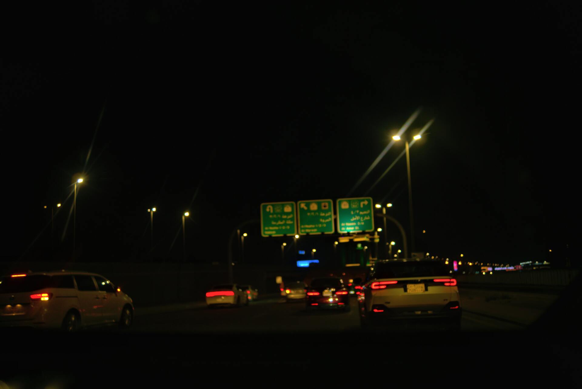 Cars on a dark highway at night with illuminated road signs and streetlights overhead.
