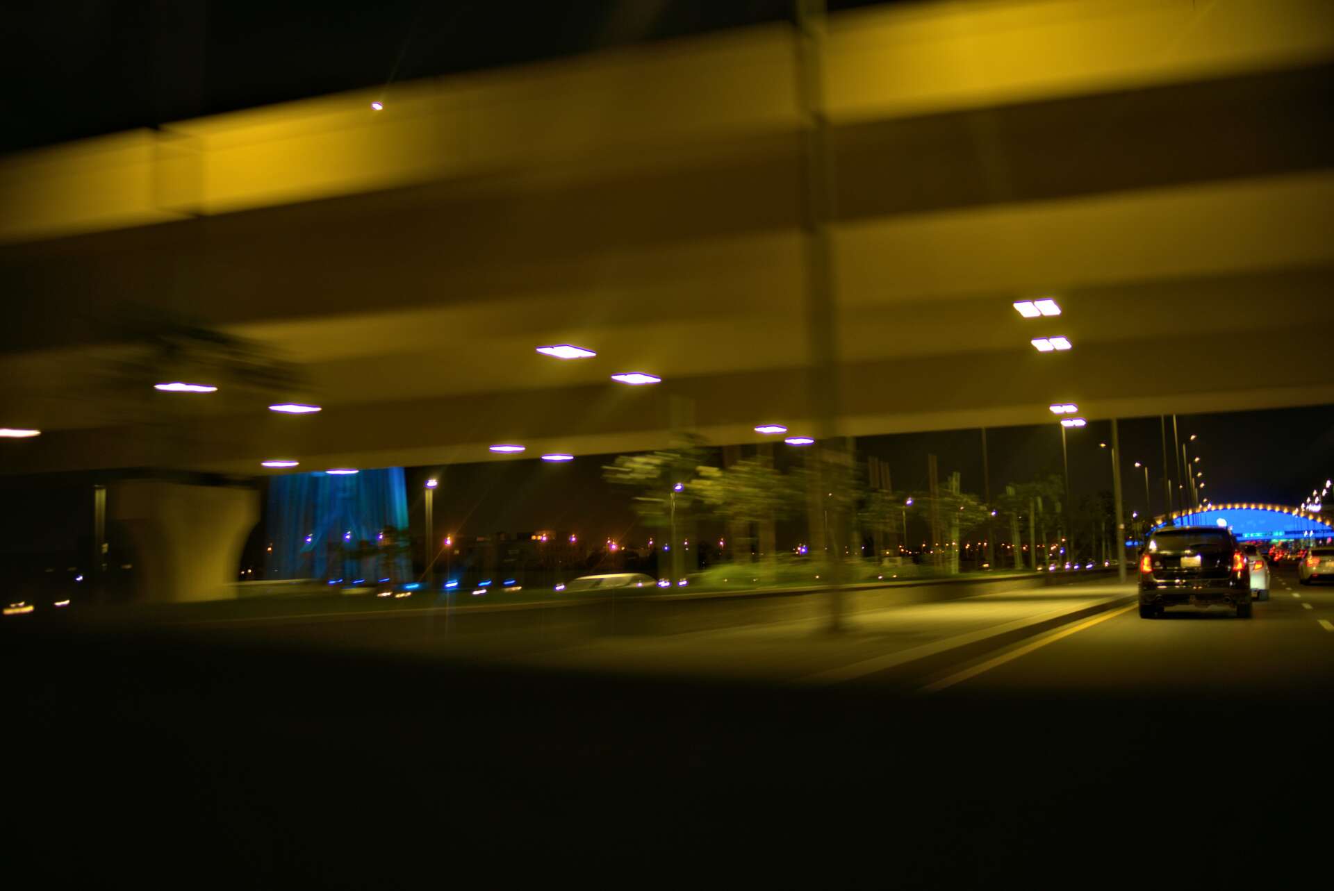 Night view of a highway underpass, with lights illuminating the road and a passing car.