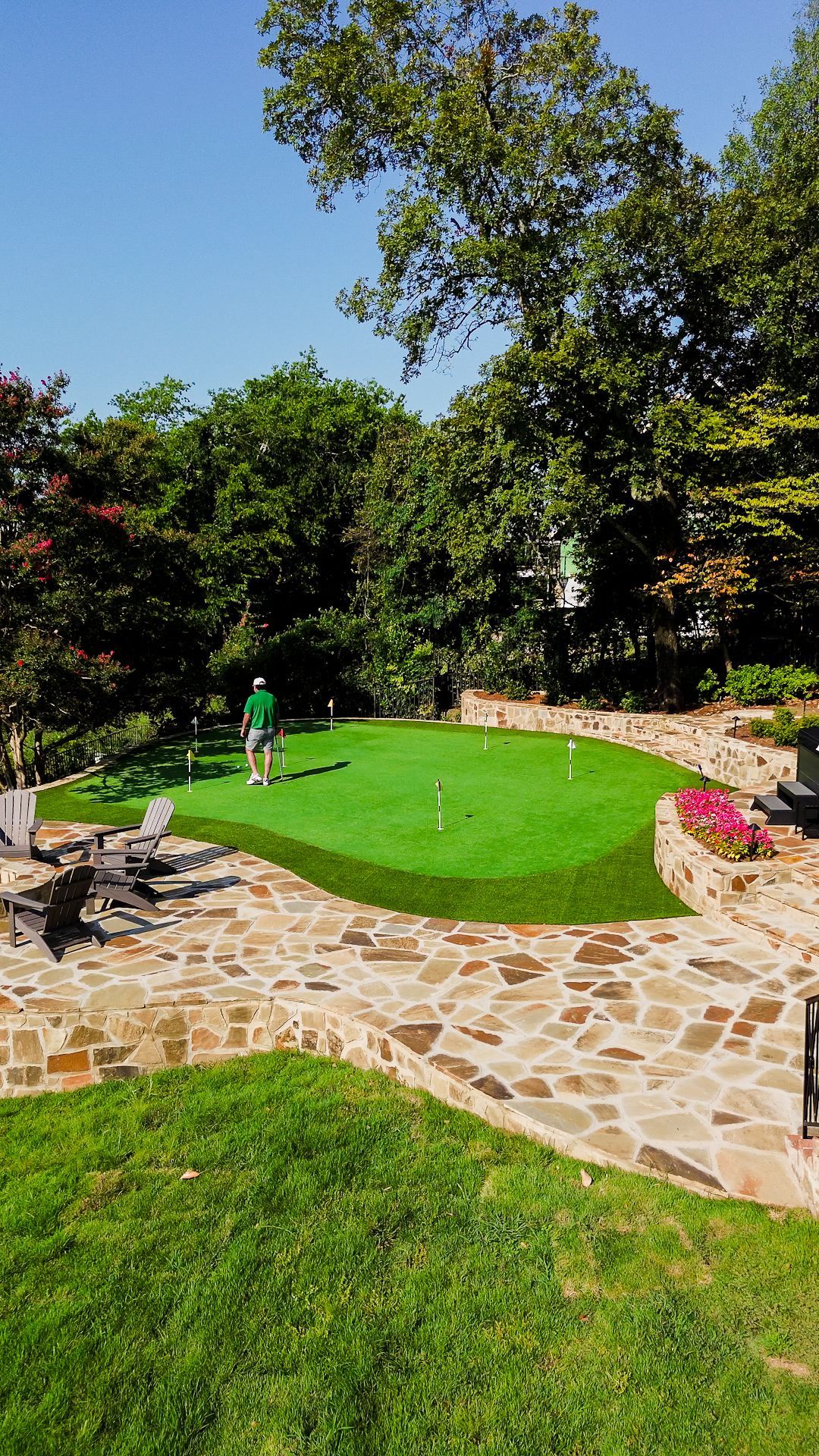 Landscaped garden with a stone path, bright green lawn, and a person standing near a small putting green.