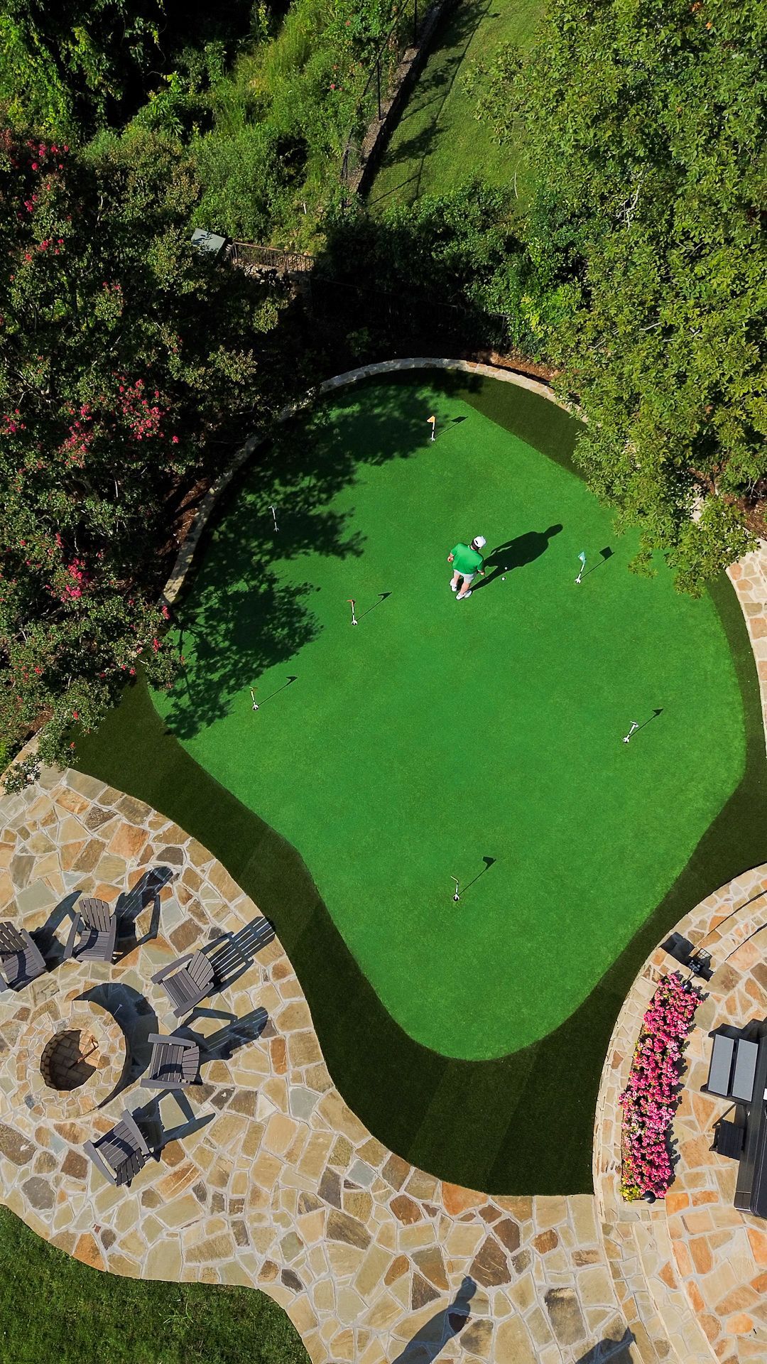 Person on a bright green mini-golf putting green surrounded by stone paths and trees