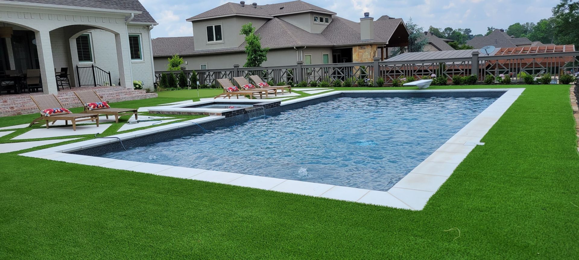 Backyard with a rectangular swimming pool, green lawn, and patio seating beside houses