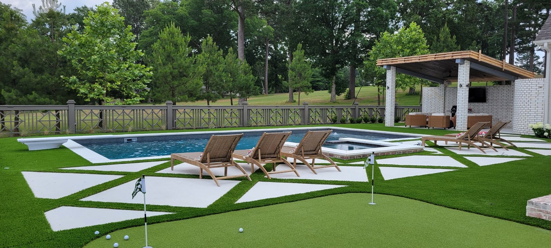 Modern backyard patio with lounge chairs, white stone pavers, and a small covered pool near a wooden fence