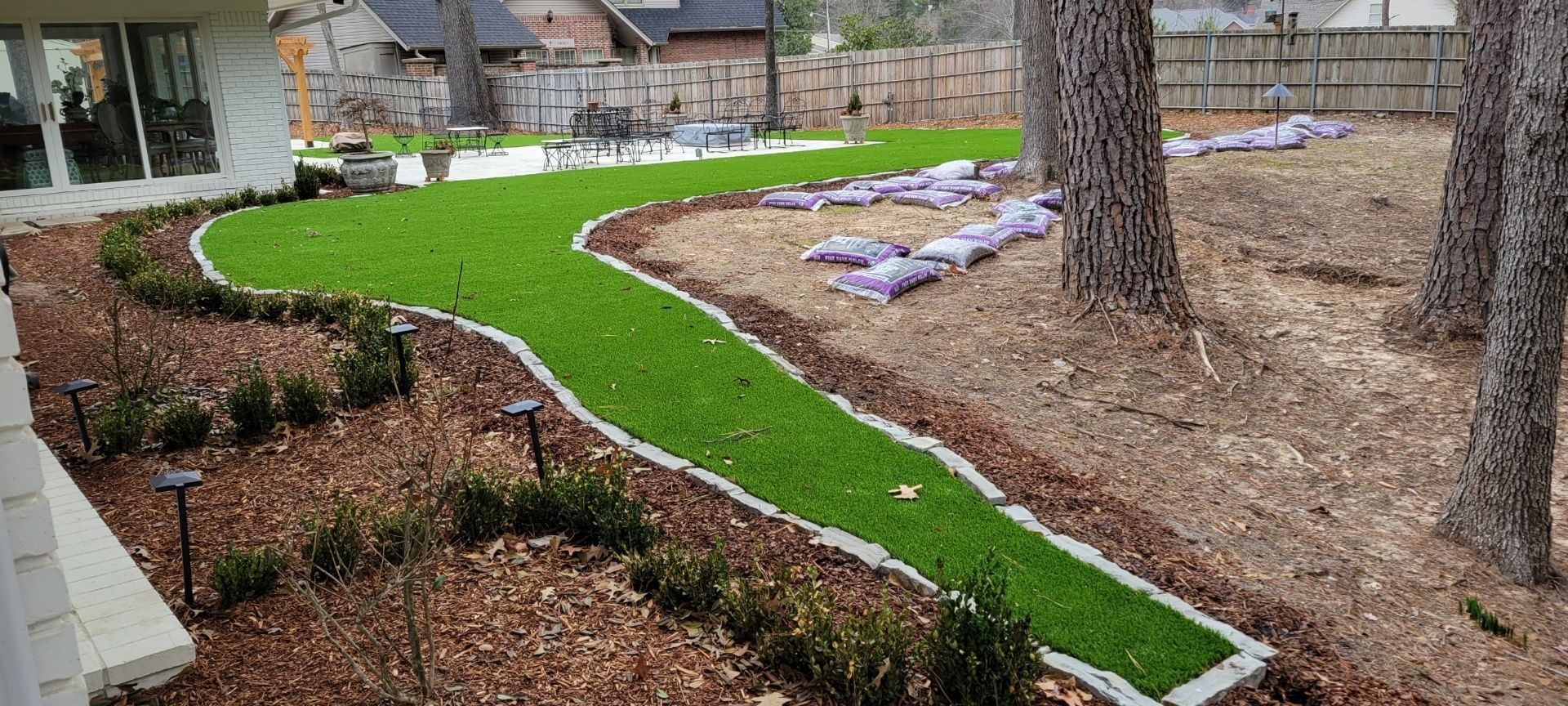 Green garden path curving through mulched landscape with trees and raised flower beds