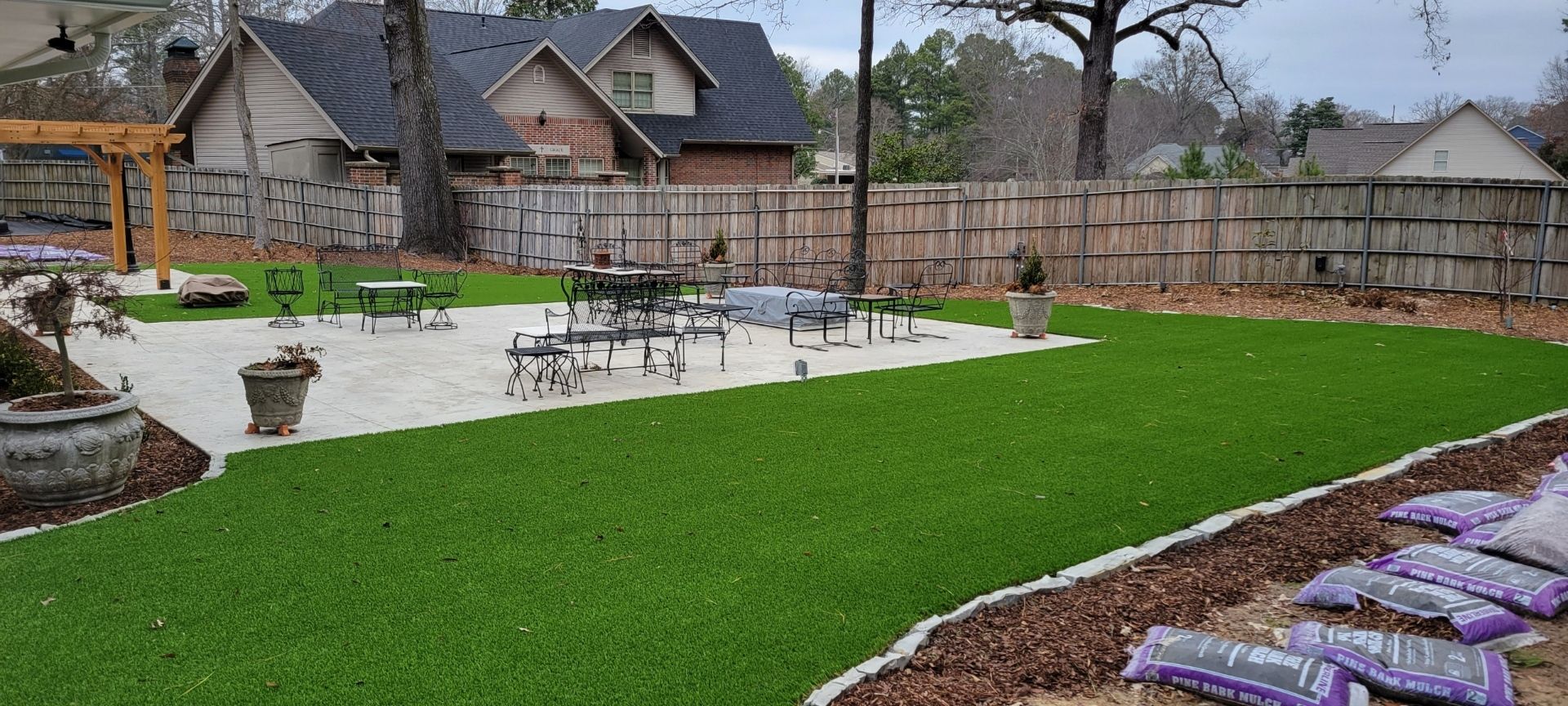 Backyard with bright green lawn, patio seating, stone wall, and landscaped garden beds