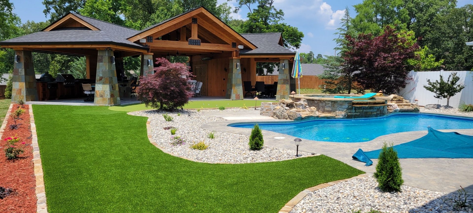 Modern wooden house with landscaped garden and blue swimming pool under a clear sky
