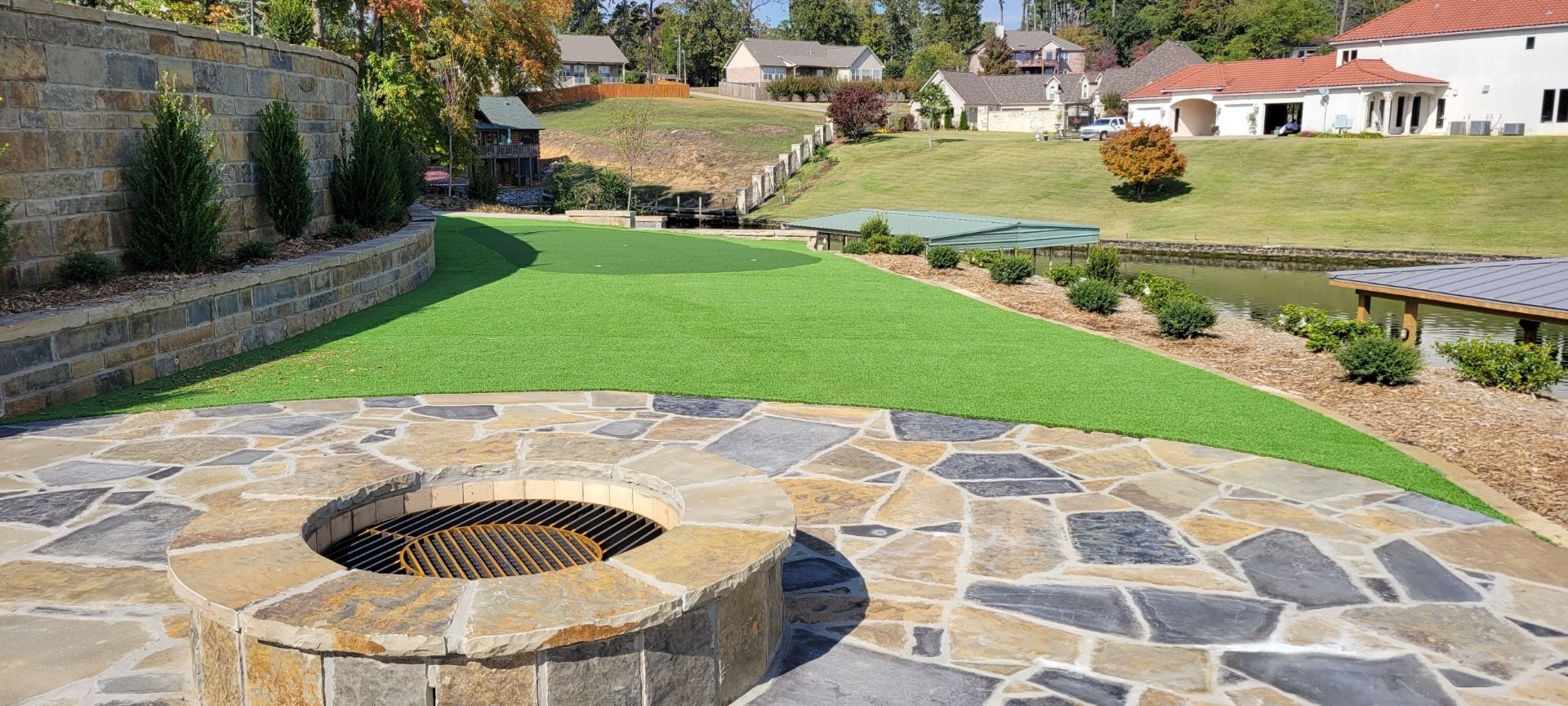 Stone patio with circular fire pit overlooking a grassy yard and houses in the distance