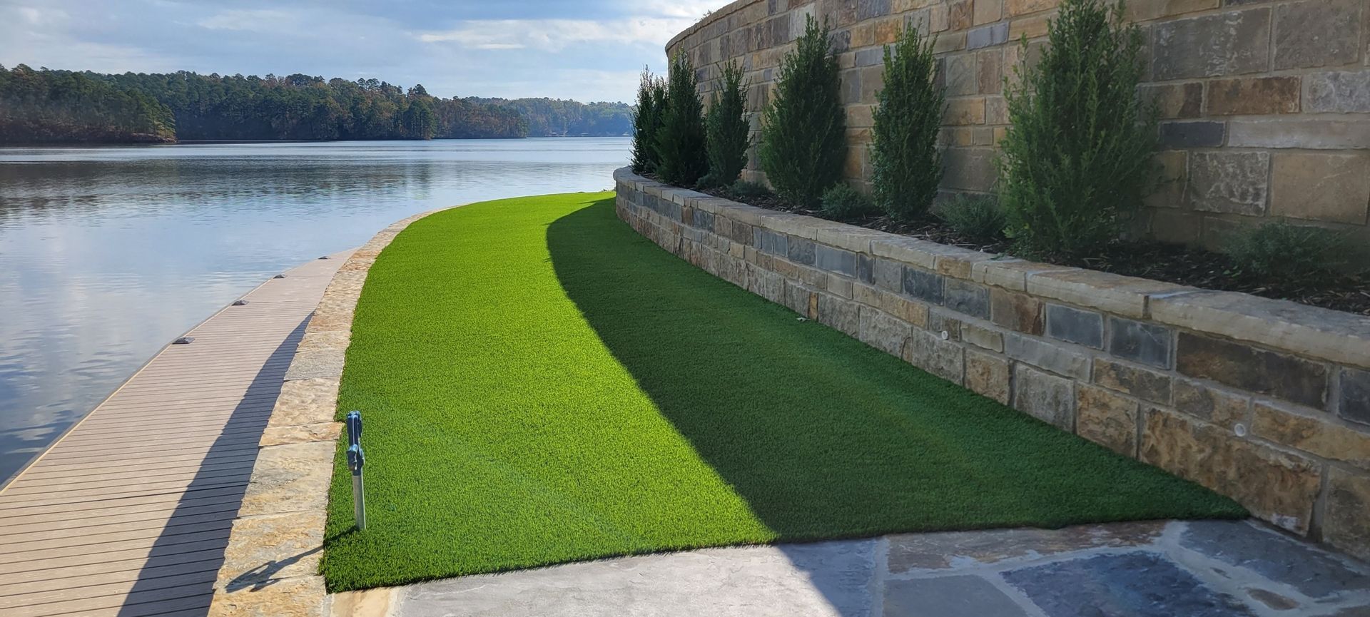Curved lakeside walkway with bright green grass beside a stone wall and calm water