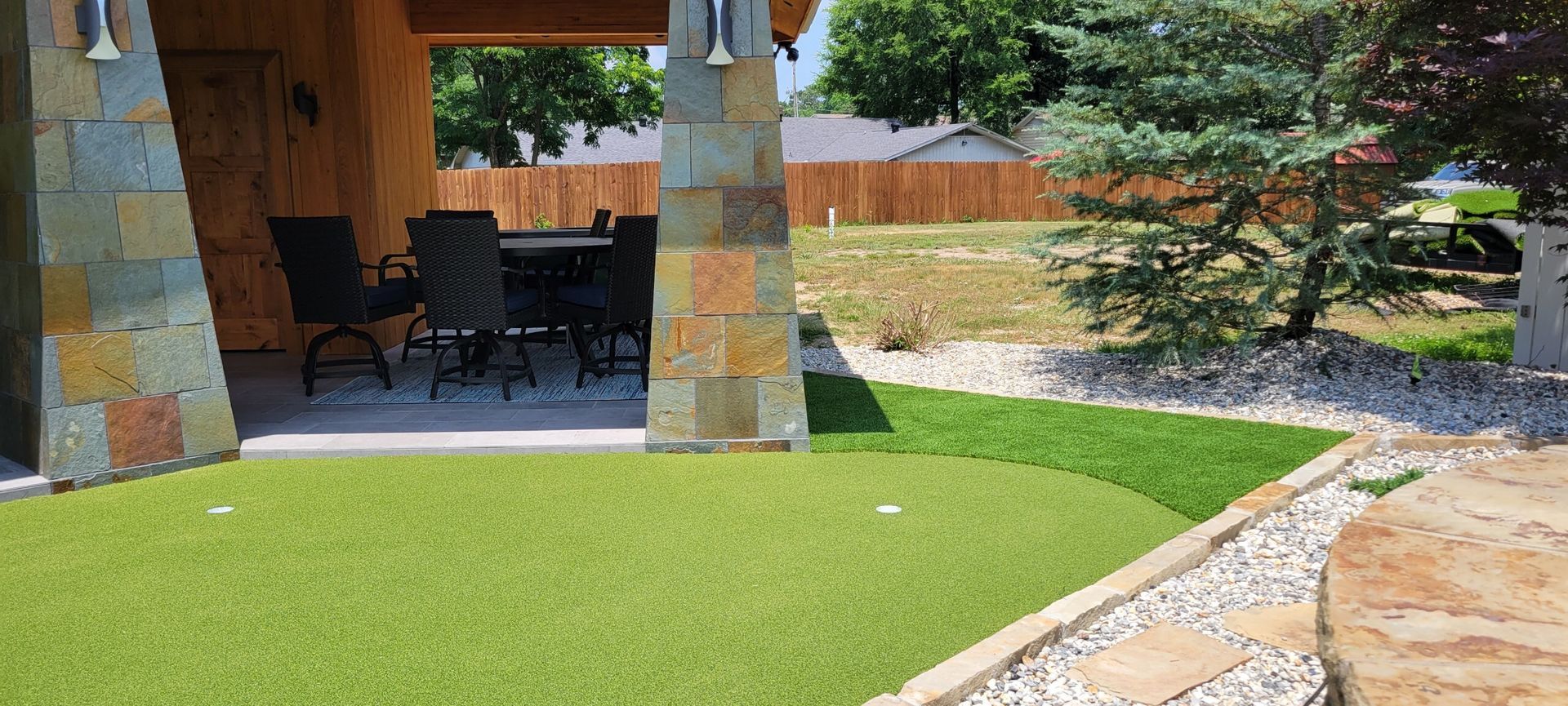 Covered patio with stone columns, outdoor seating, and a green lawn beside a stone walkway