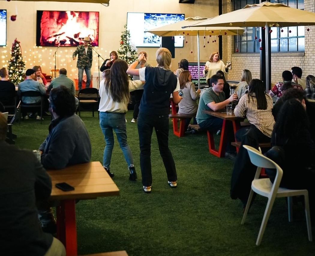 People socializing at outdoor café tables under umbrellas in a courtyard with grass and wall art