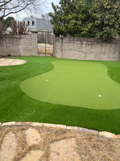 Backyard putting green with artificial turf, stone border, and a closed gate in the background