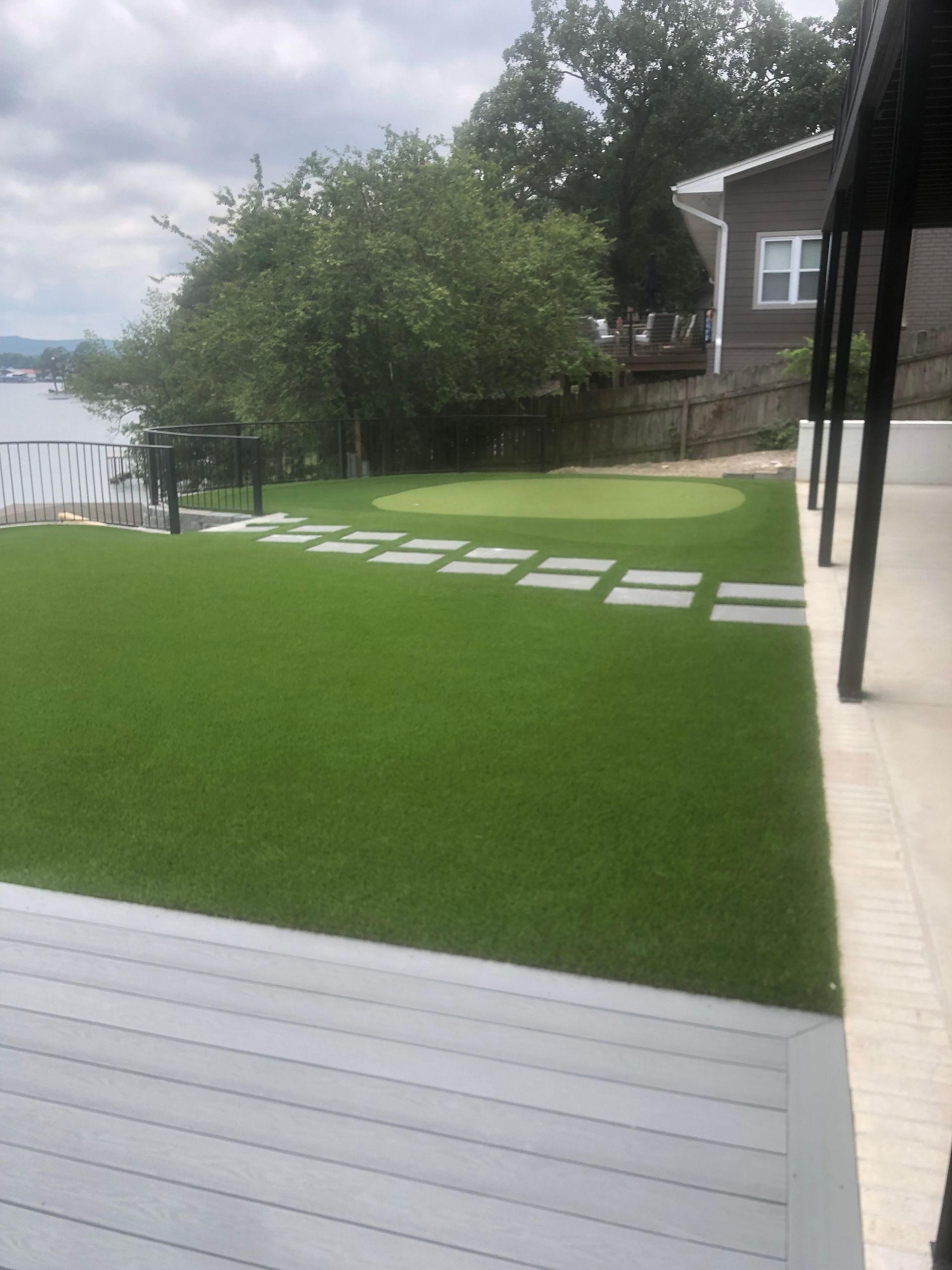 Backyard with bright green lawn, white stepping stones, and a lake view beside a house.