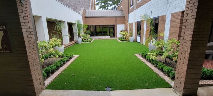 Courtyard with bright green lawn, brick buildings, and garden beds around a central walkway