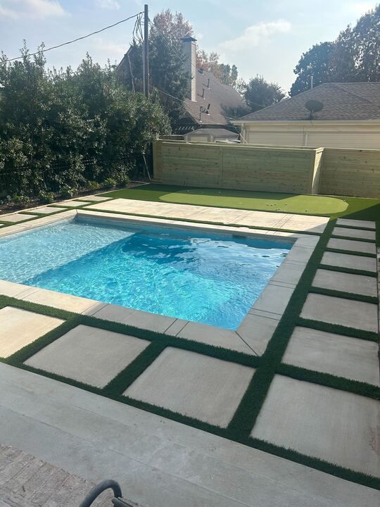 Modern backyard pool with blue water, green turf, and large gray stepping stones