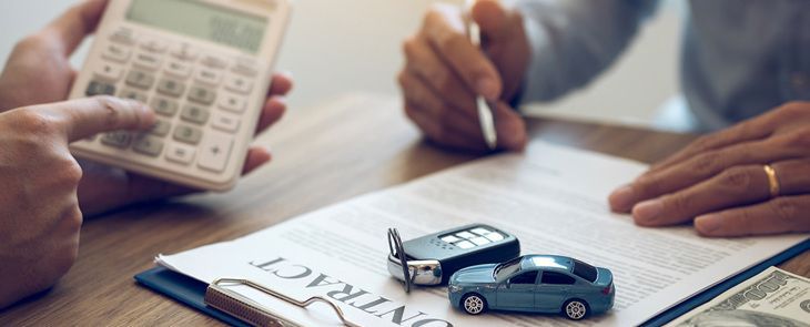 Mãos com calculadora e caneta revisando documentos de seguro de carro com dois carrinhos de brinquedo em uma mesa.
