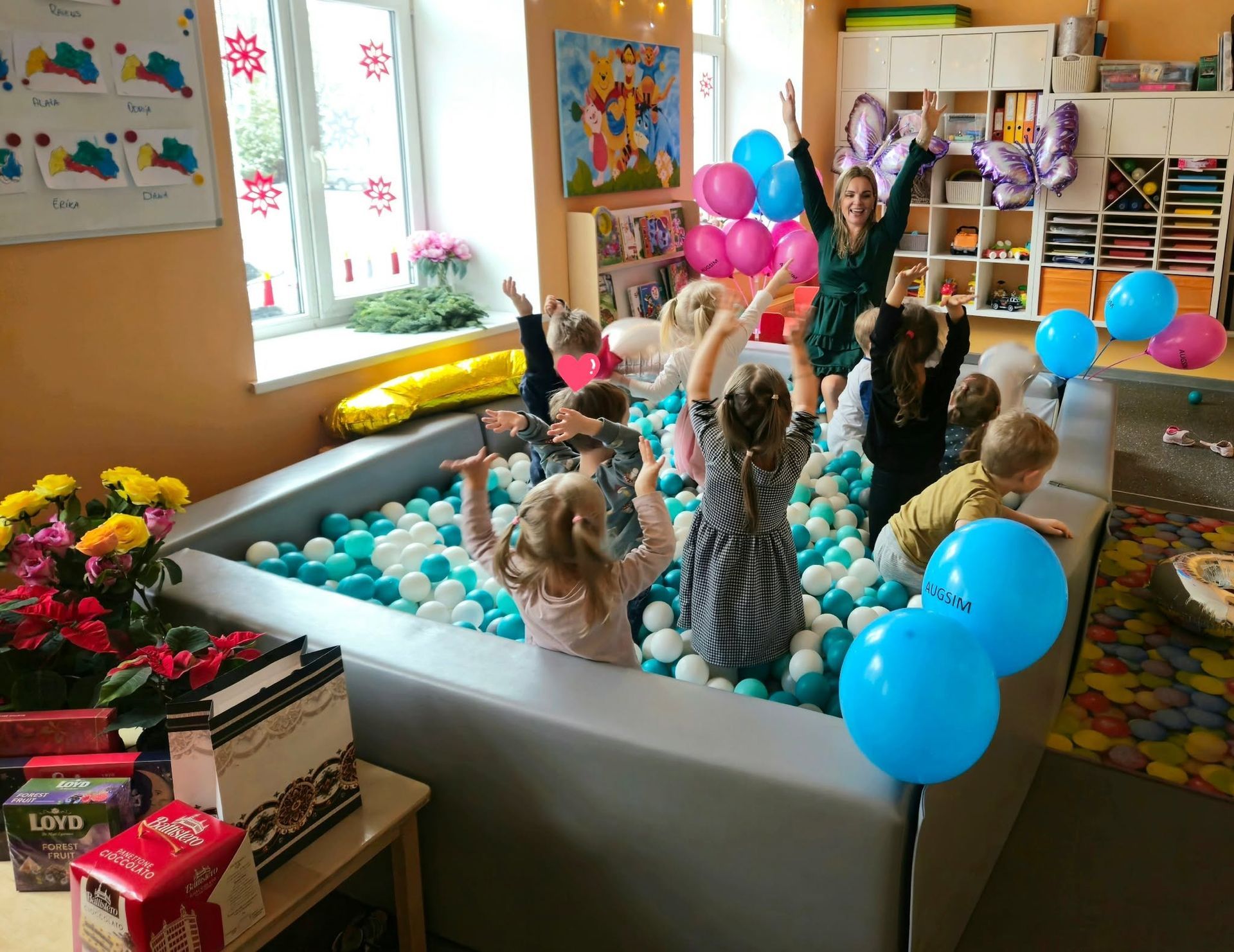 Krāsains klases eksponāts ar plīša dzīvniekiem, baloniem un dekorācijām ap lielu baltu vannu