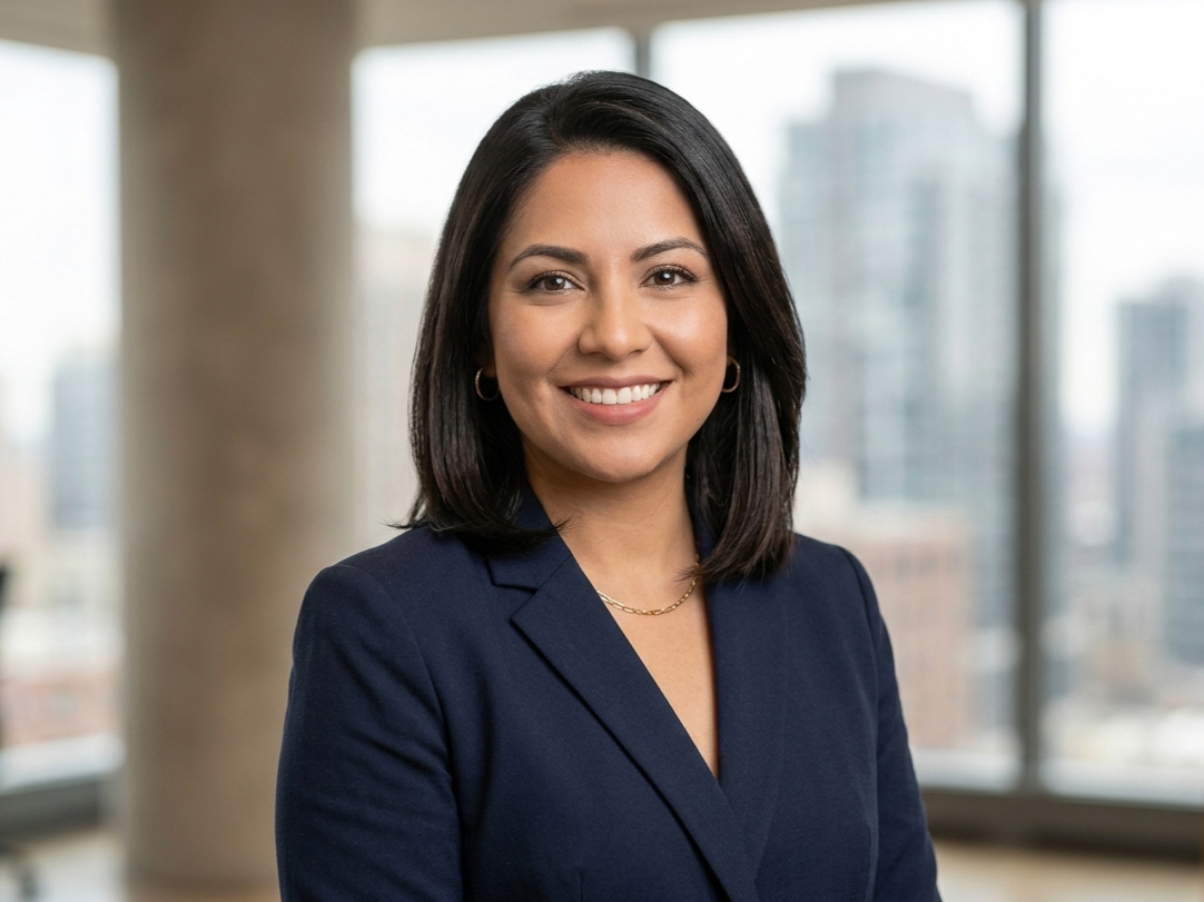 Smiling professional in a navy blazer standing in an office with blurred windows behind her