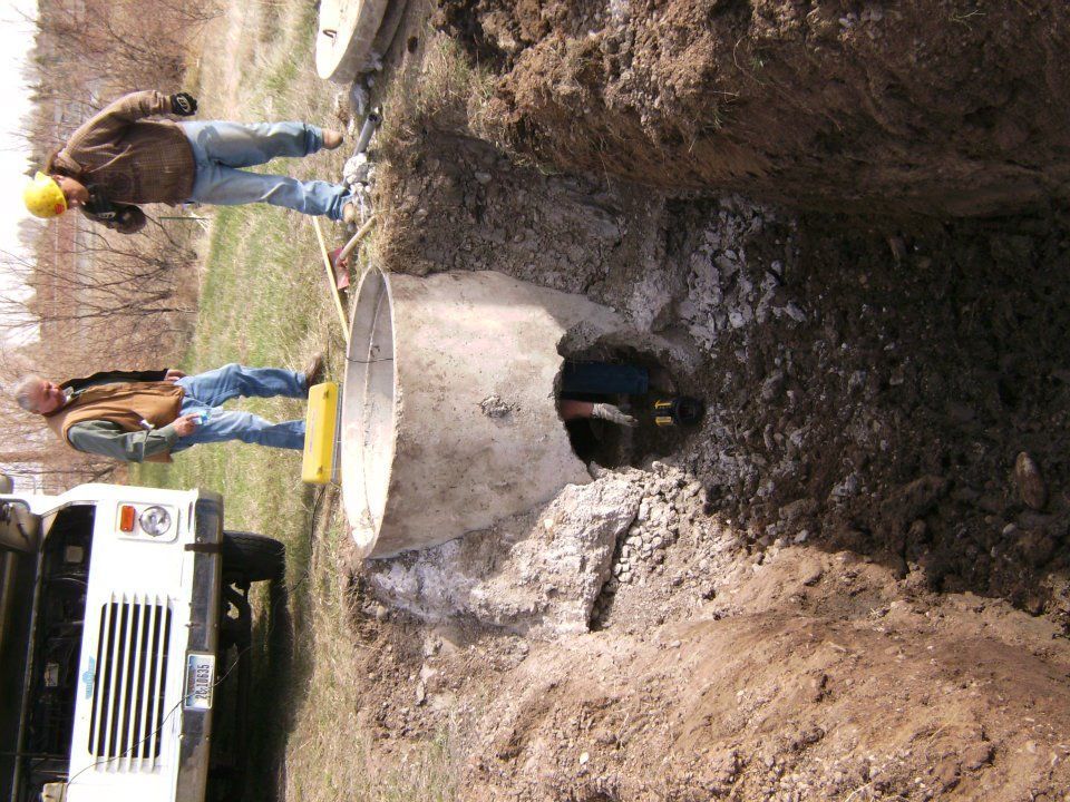 Workers at a muddy construction site beside a large excavator hole
