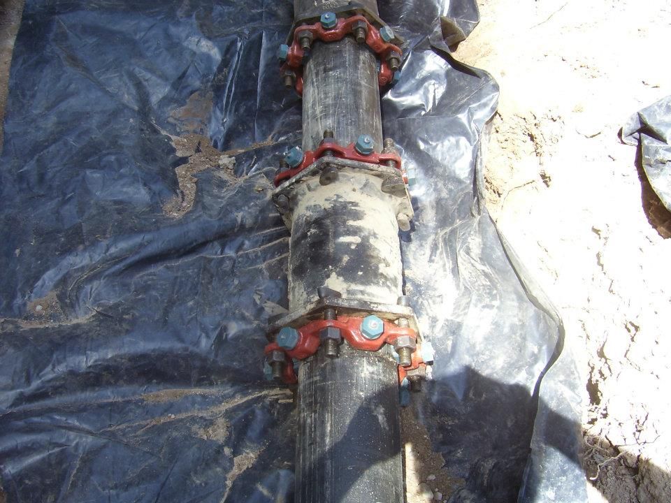 Black pipeline with a red metal coupling lying on a tarp and dirt ground.