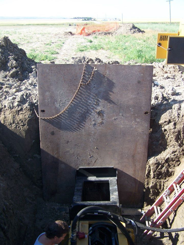 Large steel pipe segment being lowered into a trench at a construction site, with workers and equipment nearby