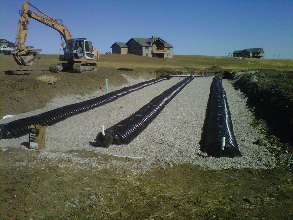 Construction site with excavator and black drainage pipes laid on gravel in a grassy field