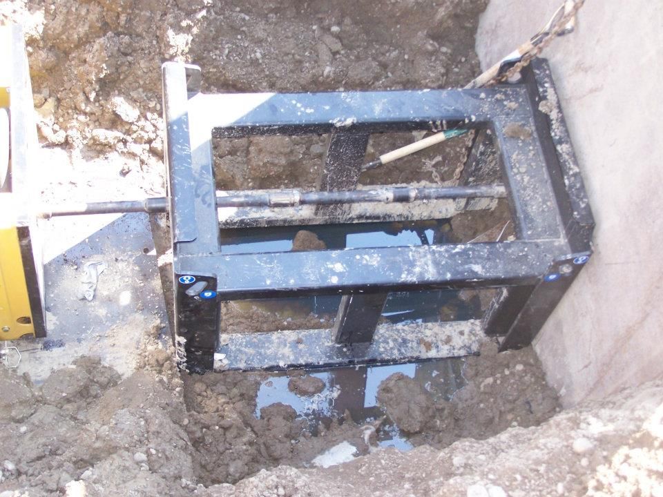 Black metal frame in a dirt trench beside a wall, with white paint splatters.
