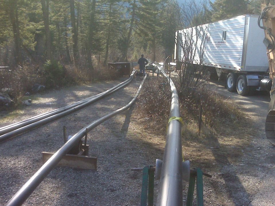 Pipeline construction along a wooded road beside a white truck and workers