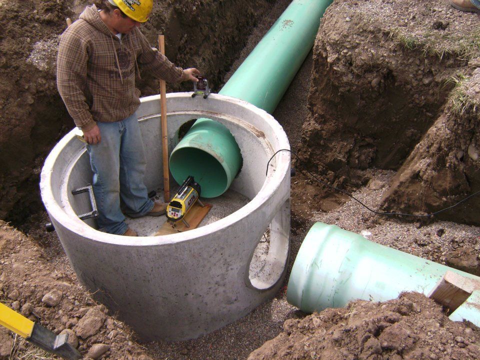 Worker installing a large green pipe into a concrete manhole at a construction site