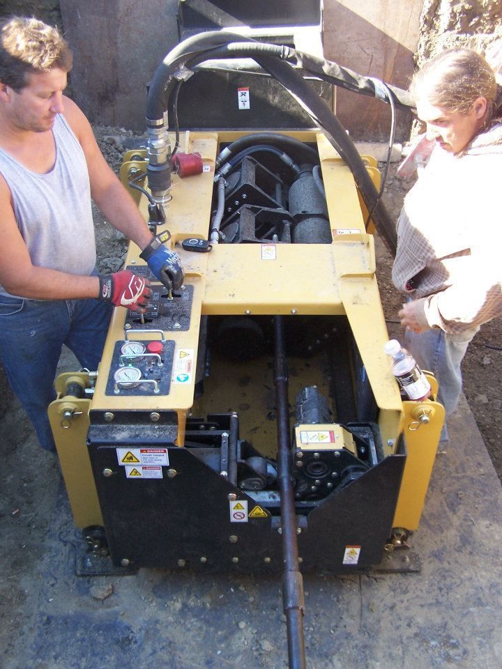 Two people inspecting a yellow and black machine outdoors, with its engine compartment open.