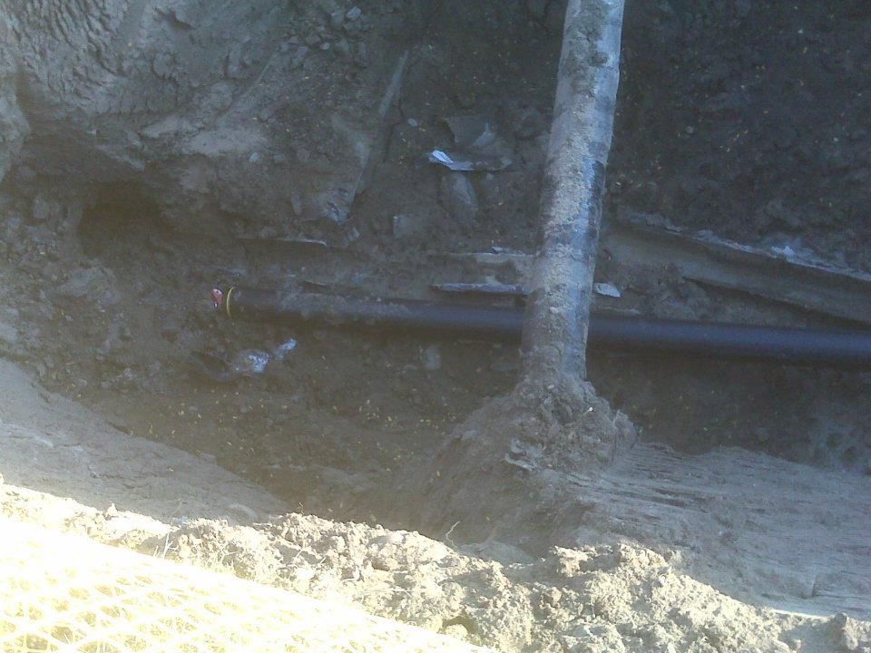 Mud wall with a small tree trunk and dark pipe in a shaded outdoor area.