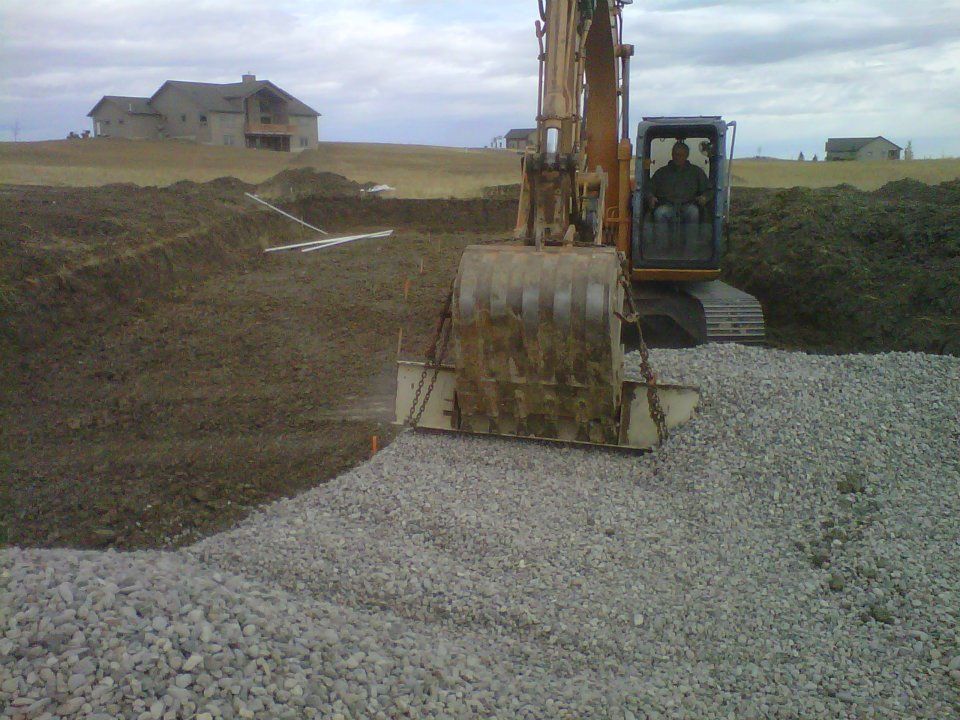 Excavator on a gravel base at a construction site with houses in the background.