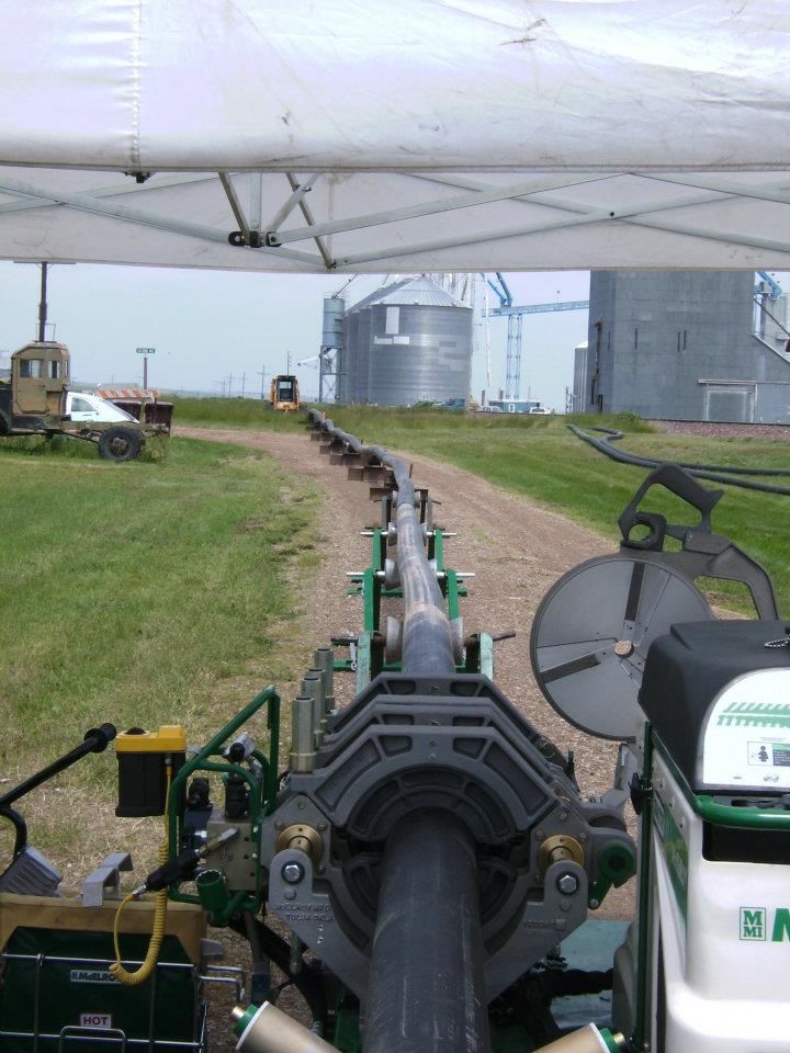 View from a vehicle on a farm lane beside large silos and equipment under a cloudy sky