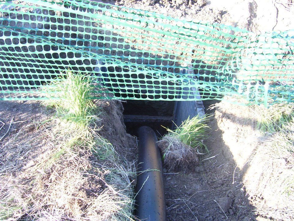 Drain pipe in an eroded trench under green safety netting, with grass on both sides.