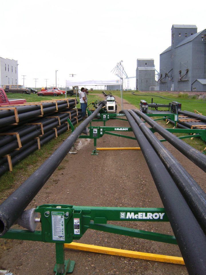 Black pipelines on green supports in an industrial yard with buildings in the background