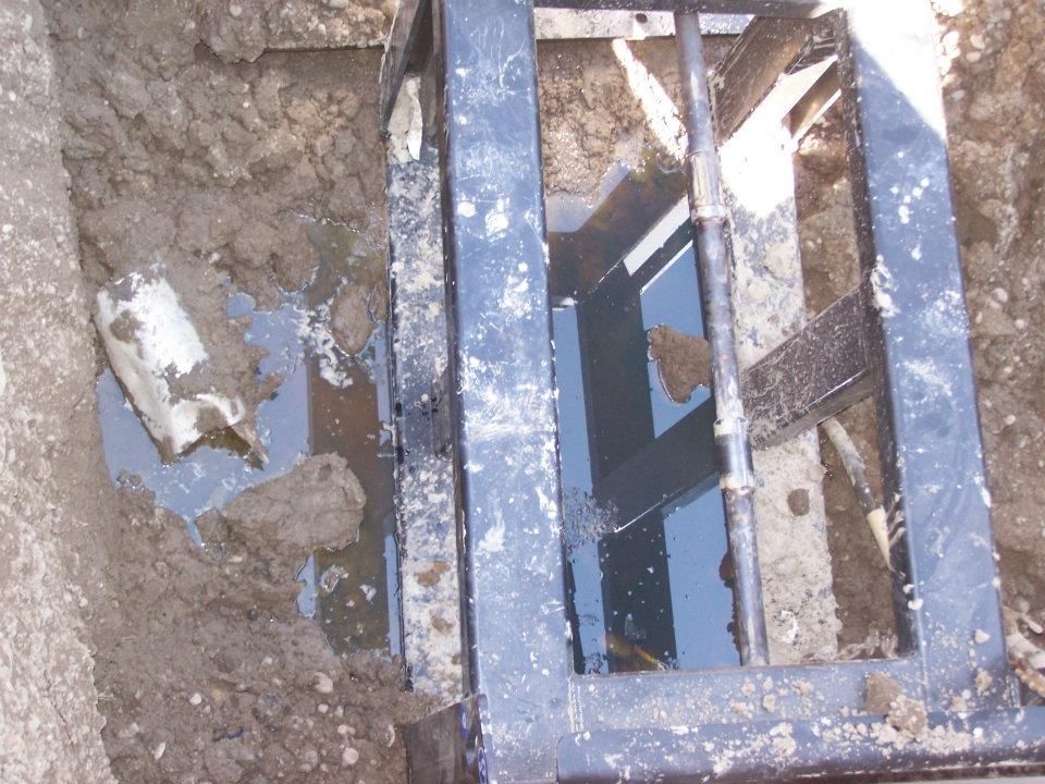 Close-up of a muddy broken blue metal frame with a rusted grill or grate in a hole in the ground