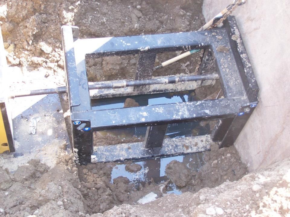 Blue metal gate lying in a muddy excavation beside a concrete wall