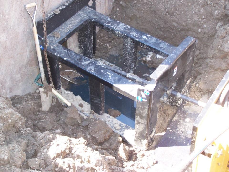 Metal support frame in a dirt trench beside a wall, with tools and construction debris nearby