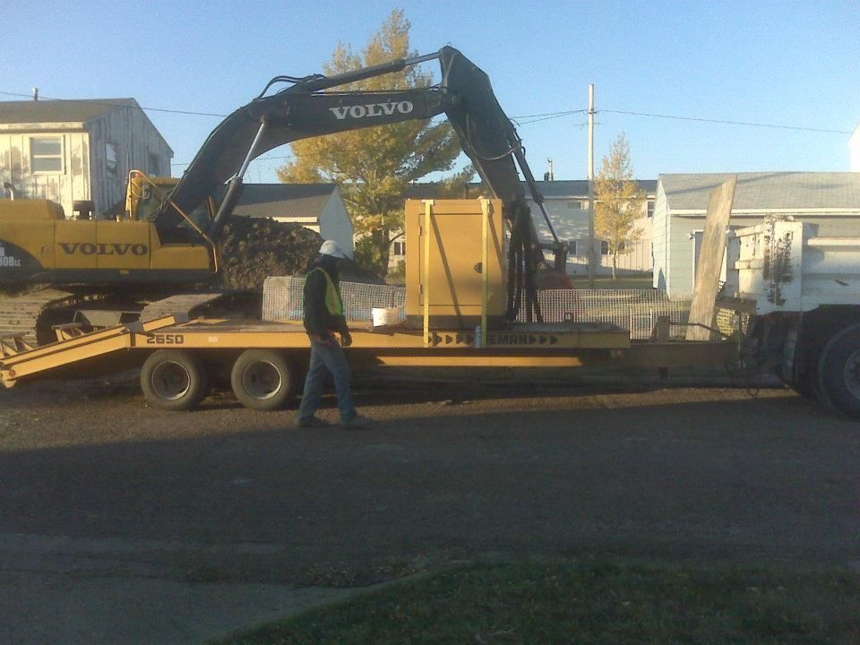 Yellow Volvo excavator loaded on a flatbed trailer, with a worker standing beside it outdoors.