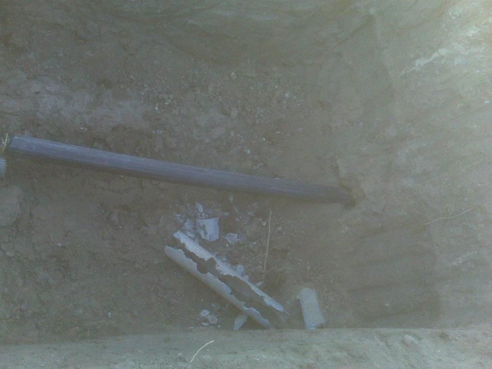 Broken pipes and debris in a muddy trench or excavation site.