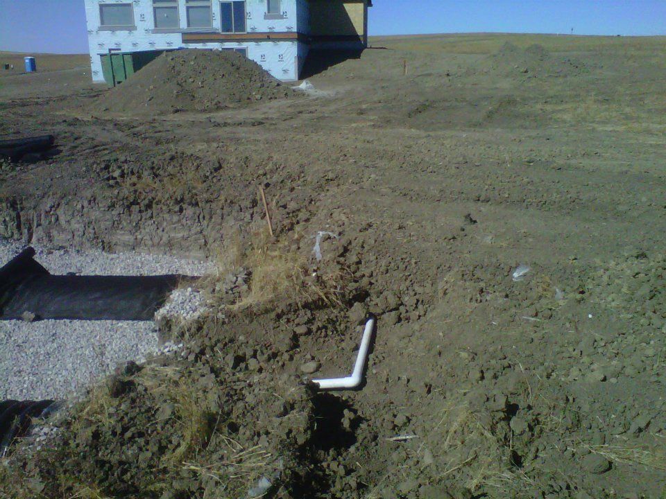 Construction site with dirt mound, concrete trench, and a white pipe near a house.