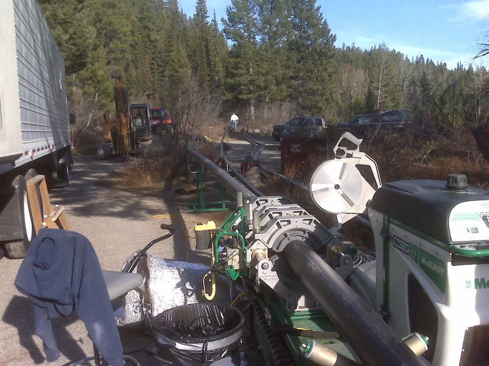 Logging equipment and machinery on a forest road under tall pine trees, with hoses and a tractor visible